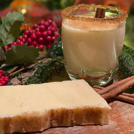 Rum and Eggnog fudge with a glass of eggnog and cinnamon sticks. Christmas decor in the background